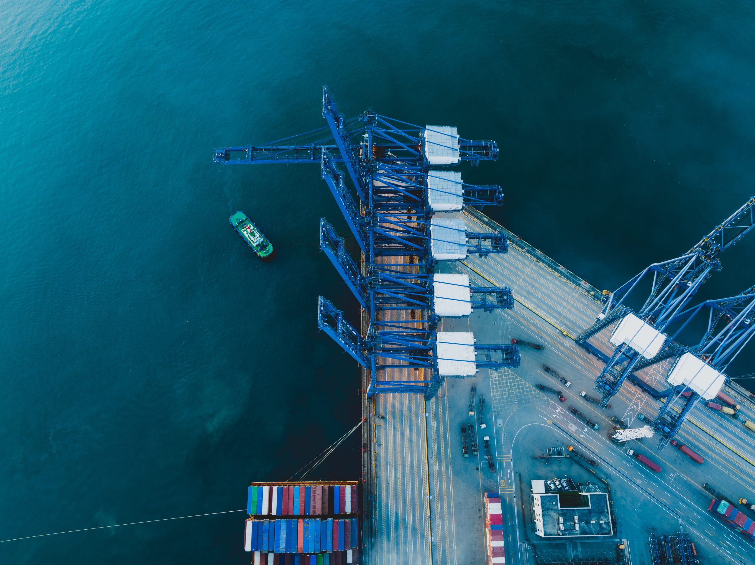 High-angle aerial view of a blue-toned shipping terminal and cargo cranes, symbolizing the structural resilience and continuity of global supply chains.